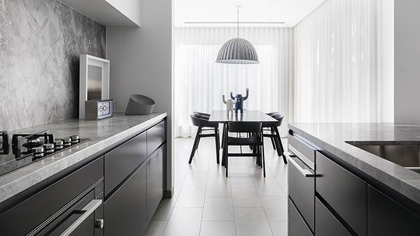 Kitchen with black cabnitery looking through to a black dining table on a backdrop of white floor length curtains.